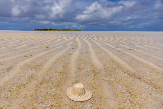 Boat tour visitors explore Honeymoon Island in Aitutaki while a hat rests on the sandy beach under a cloudy sky