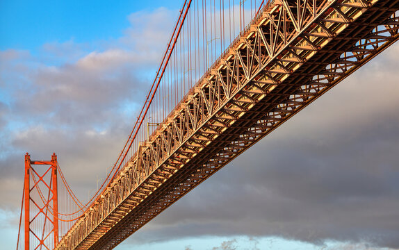 View of 25 April Bridge spanning Tagus River with steel structure and cables seen from low angle in Lisbon, Portugal