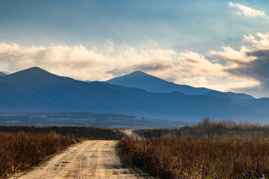 Road leads to mountain range in winter with clouds and blue sky in the background in Romania