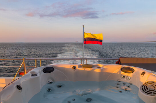 Relaxation in a hot tub on a boat with a Colombian flag while traveling over water at sunset