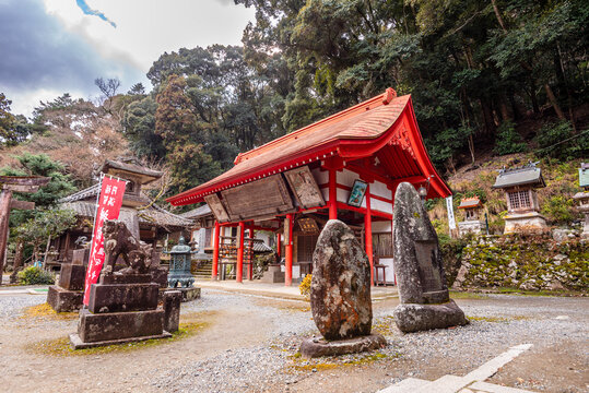 Front view of a vivid red torii gate with stone statues on gravel ground in a forest during daytime in Japan