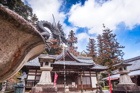 Dragon-shaped purification fountain in Ryuanji Temple with tiled roof and lanterns under blue sky in Osaka
