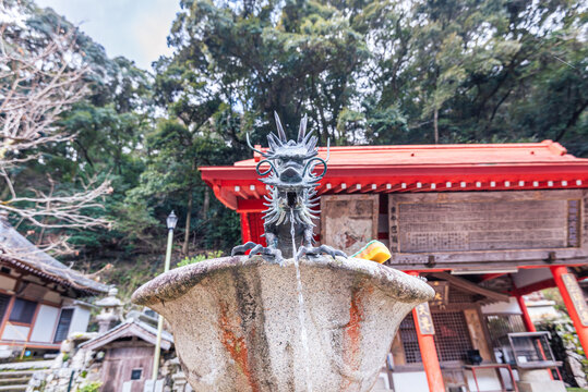 Close-up view of dragon-shaped fountain at Kumano Sansho Gongensha with red-roofed shrine buildings in Minoh, Japan