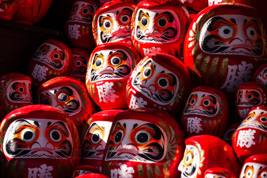 Vibrant red Daruma dolls clustered with bold expressions and kanji for victory at Katsuo-ji Temple in Minoh, Japan