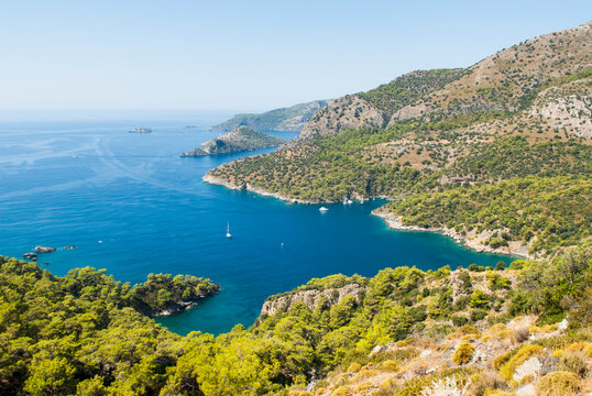 Lycian coast features clear water and green hills with boats near an island in the distance in Turkey