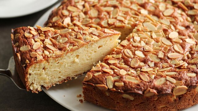 Homemade almond cake slice on a serving spatula with toasted nut topping on a plate.