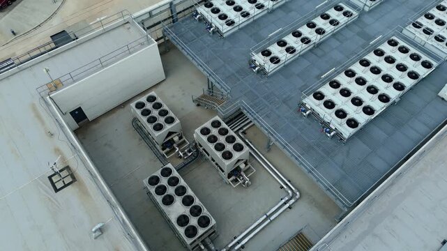 Close-up aerial orbit shot of industrial rooftop HVAC cooling fan banks on warehouse building