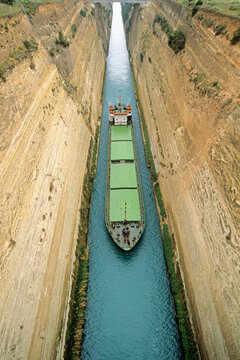 Large cargo vessel navigates through bold cliffs of Corinth Canal in Greece during daytime