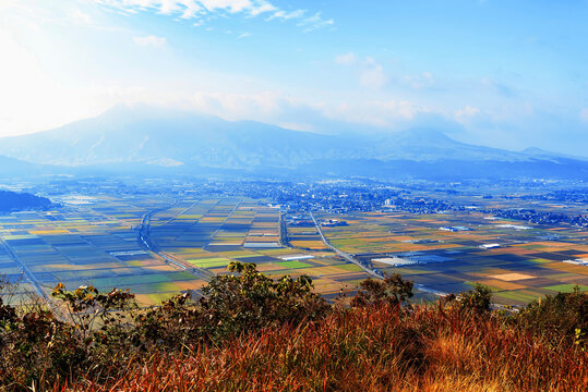 Autumn colors cover the countryside in Aso region, revealing fields and distant mountains in a clear sky