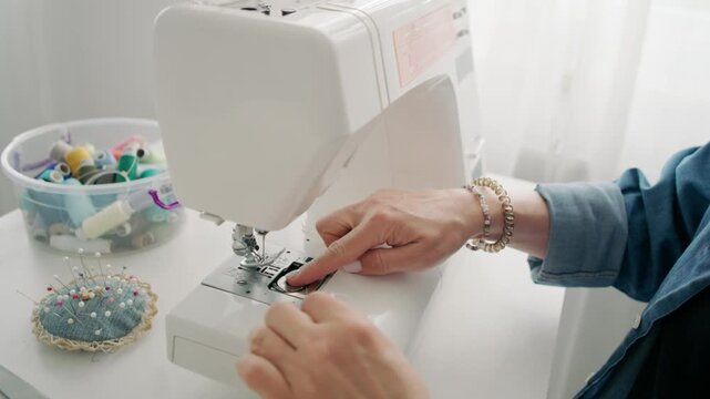 Female Hands carefully guide thin thread through sewing machine needle in bright home workspace