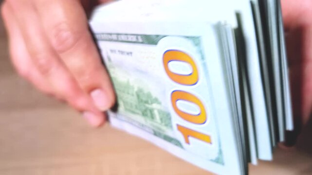 Close-up video of female hands holding and flipping through a stack of hundred dollar bills, estimating the amount and enjoying the feeling of financial wealth, success, and abundance.