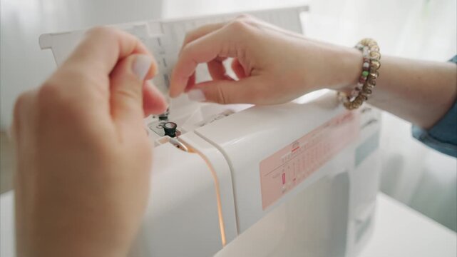 Female Hands carefully guide thin thread through sewing machine needle in bright home workspace