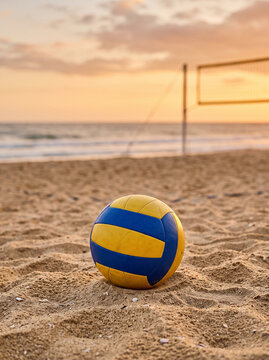 yellow and blue volleyball ball lying on sandy beach with net and sea at sunset