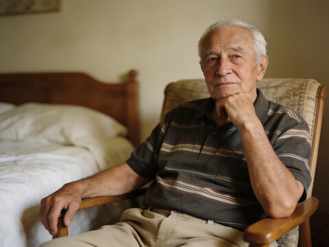 Portrait of an elderly man sitting in a chair at home, senior care and retirement concept.