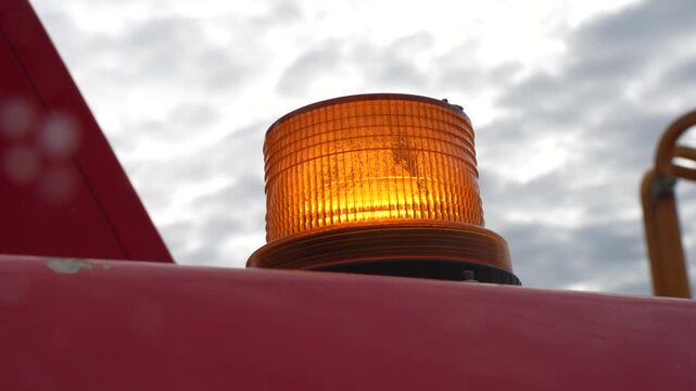 Flashing amber warning beacon light mounted on a heavy machinery roof against an overcast sky for industrial safety and site visibility
