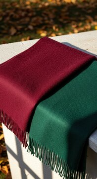 Two wool scarves in burgundy and green draped over a stone ledge. Luxury autumn accessories with fringe. Seasonal winter textiles