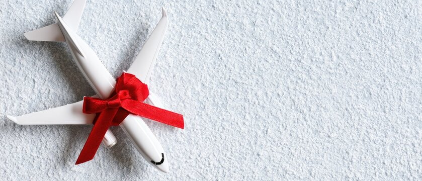 White model plane wrapped in a red ribbon sits on a surface covered in artificial snow with soft lighting creating shadows