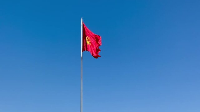 The red and yellow flag of Kyrgyzstan in the blue sky