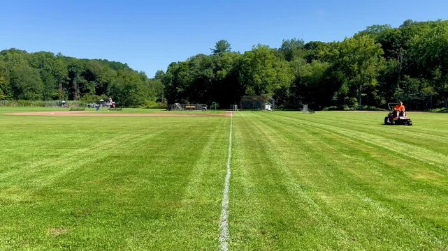 Riding lawn mower cutting grass on sports field with painted line