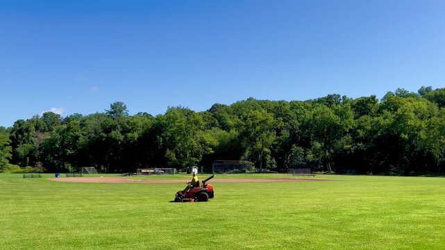Riding lawn mower cutting grass on a large green sports field
