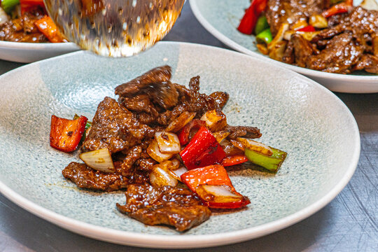 Professional chef hands tossing sliced beef and bell peppers in a hot wok for a black pepper beef dish.