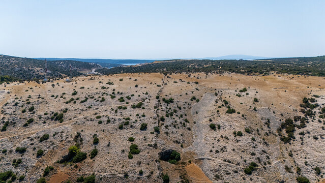 Aerial view of the rocky landscape of Rab island with sparse vegetation, a stone wall dividing the terrain, and distant sea views in Rab, Primorje-Gorski Kotar, Croatia.