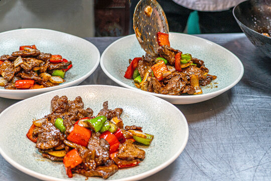 Professional chef hands tossing sliced beef and bell peppers in a hot wok for a black pepper beef dish.