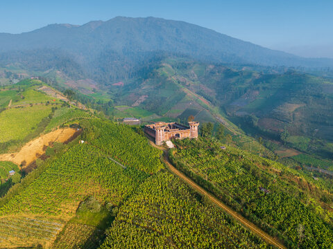 Aerial view of Mbeteng Sata fortress ruins situated on a lush green hillside surrounded by terraced agricultural fields and rolling mountains in Indonesia.
