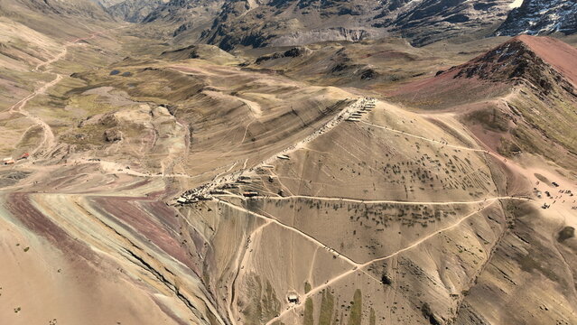 Aerial view of the colorful mineral-rich slopes of Vinicunca, also known as Rainbow Mountain, with winding hiking trails and rugged Andean terrain in Quispicanchi Province, Cusco, Peru.