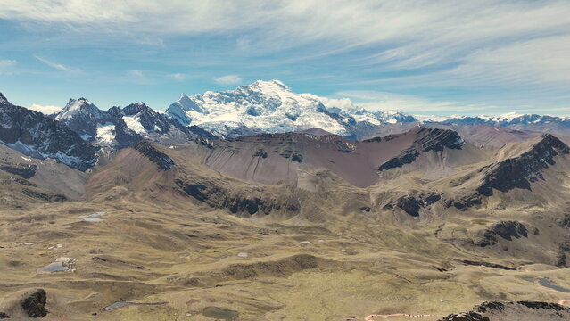 Aerial view of Vinicunca, also known as the Rainbow Mountain, featuring vibrant mineral-rich slopes, snow-capped Andean peaks, and rugged terrain in Quispicanchi Province, Cusco, Peru.