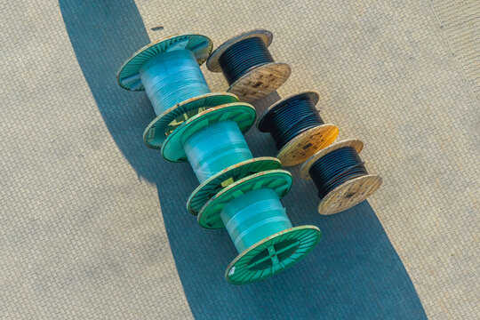 Aerial view of industrial cable reels with plastic wrapping and black electrical cables arranged on a paved surface in Poland.
