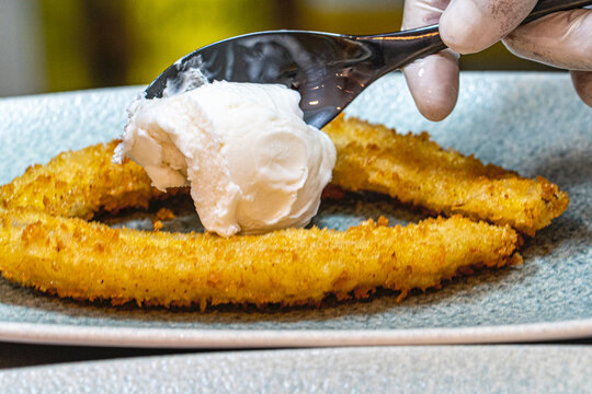  Professional chef hands plating a gourmet grilled banana dessert with vanilla ice cream and rich chocolate sauce.