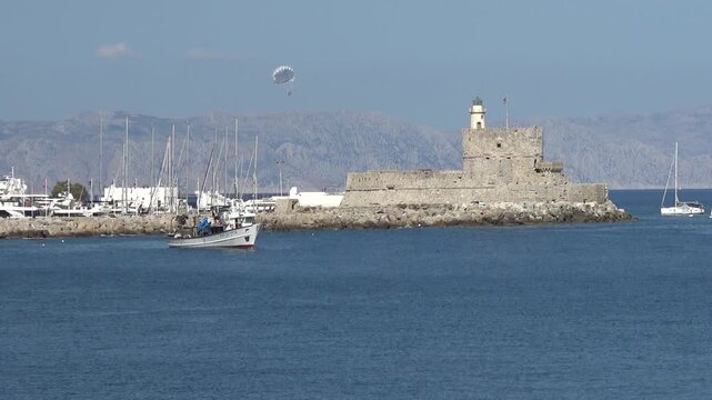 Rhodes Town, Greece - 23 of October 2023: Saint Nicholas fortress and lighthouse with parasailing in Rhodes harbor
