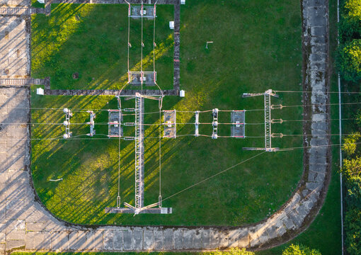 Aerial view of an electrical substation with power lines and metal structures set on a green lawn with concrete pathways in Gdynia, Pomeranian Voivodeship, Poland.