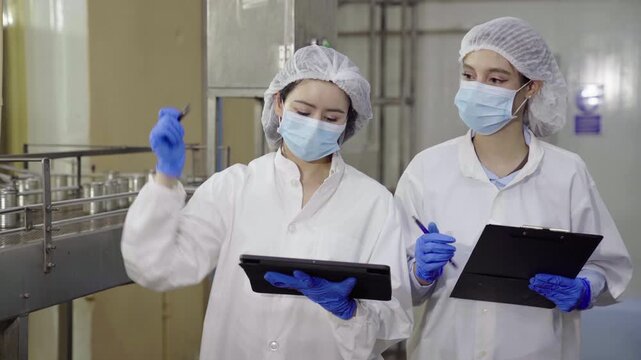 Two female inspectors checking canned food production line in plant