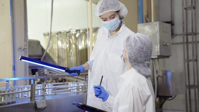 Two female inspectors checking canned food production line in plant