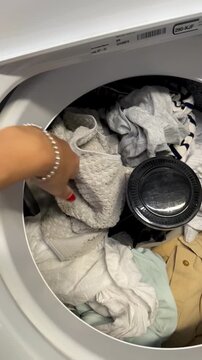 Female hand takes dirty clothes from a laundry basket and loads them into a top-loading washing machine. Vertical 4K video showing everyday laundry, household chores, cleaning and home routine