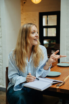 Woman Engaging in Conversation While Taking Notes in a Cozy Cafe