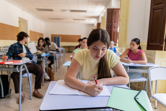 Young student writing notes in a busy classroom