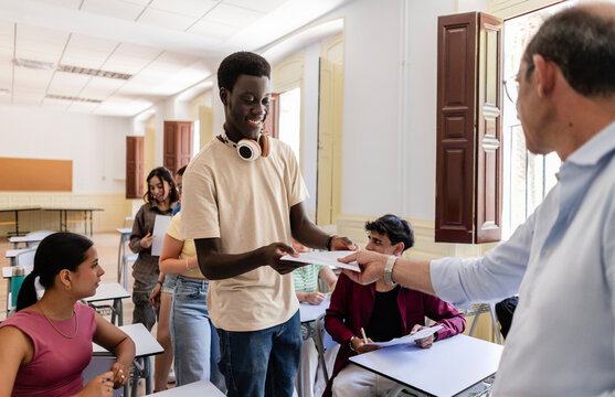 Teacher handing out test papers to smiling student in classroom