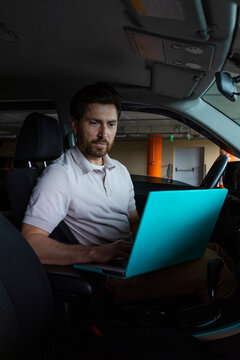 A man is working on his laptop in a parking lot.