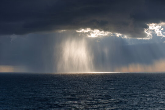Dramatic sun rays breaking through dark storm clouds over the open ocean.