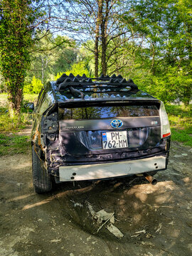 A damaged Toyota Prius hybrid car with a large dent in the fender and a missing bumper is parked in the woods near Tbilisi; accident damage and body damage to the car, Georgia 10.04.2025