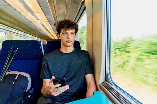Young Man Sits on Train While Using Mobile Phone