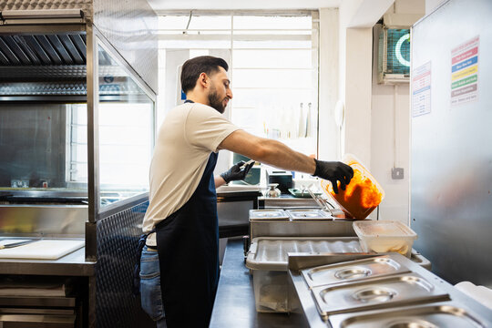 Chef pouring fresh red sauce into a container in a commercial kitchen