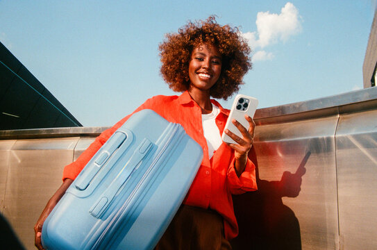 Woman holding smartphone with blue suitcase for travel