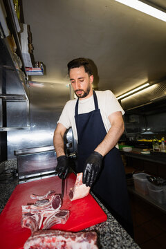 Professional chef butcher slicing raw lamb chops in a kitchen
