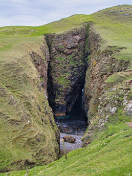 A dramatic natural rock arch and narrow sea inlet cut through grassy cliffs north of Malcolms Head on Fair Isle UK