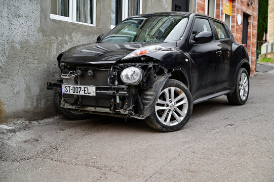 Damaged black Nissan Juke SUV without bumper and grille parked in Tbilisi, car with front-end damage, Georgian license plate, capital region, Georgia 15.4.25