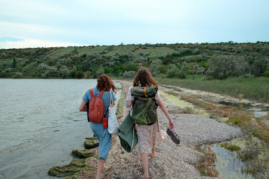 Two women walking along the shoreline with backpacks